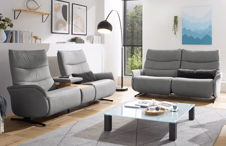 Modernes Wohnzimmer mit grauen Relaxsesseln und Sofa, stilvoll eingerichtet mit Glas-Couchtisch.